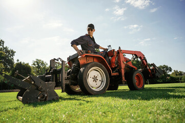 Obraz premium Loan work. Man is with utility tractor with grass cutter and aerator equipment on the field