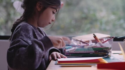 A happy little girl drawing and coloring with a blue pencil at her desk