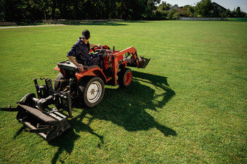 Loan work. Man is with utility tractor with grass cutter and aerator equipment on the field