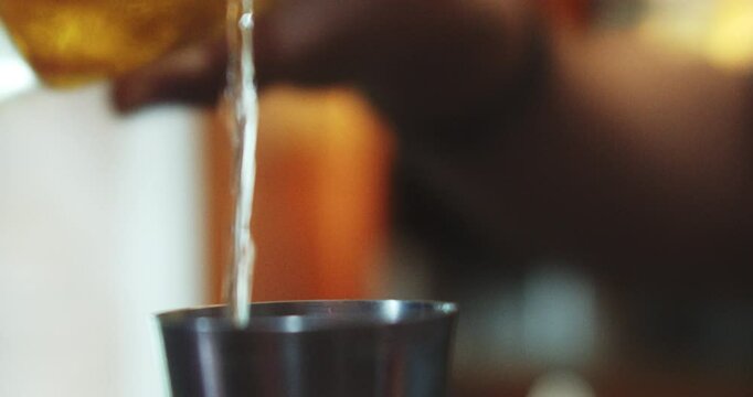 Beautiful slow motion shot of a shot of tequila being poured from a bottle into a measuring cup to prepare a Mexican cocktail in a restaurant.
