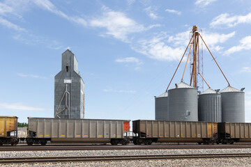 A freight train passing grain silos cloudy sky © Cavan