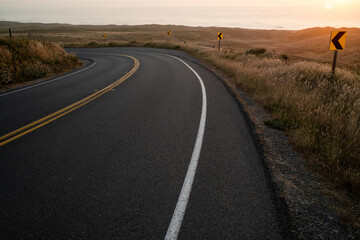 Fototapeta premium Curving roadway wrapping around hills on the coast during sunset