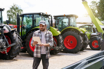 Agribusiness. Agricultural and construction equipment dealer. Man stands against new tractors and...