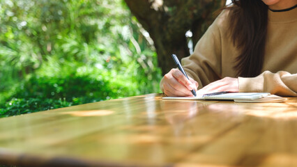 Closeup image of a woman writing on a notebook on wooden table