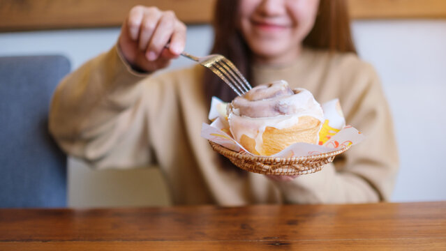 Closeup image of a young woman holding and eating cinnamon roll with fork