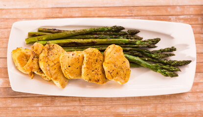 Fried chicken breast pieces with asparagus on white plate