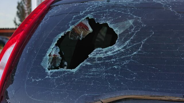 Cracks expand across a broken rear car window, highlighting damage. The vehicle remains parked outside a home, showcasing the risks of vandalism and potential safety hazards