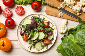 Healthy vegetarian food. Plate of salad and vegetables on light wooden table, flat lay