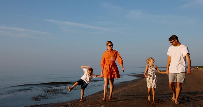 young family with two children walk on the beach coast of the baltic sea at sunset