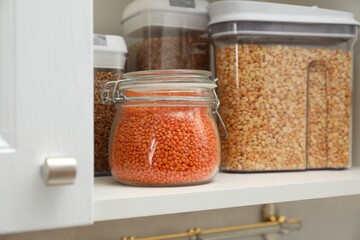 Different types of cereals and legumes in containers in closet, closeup