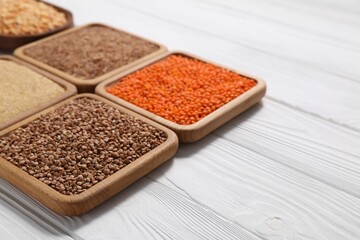 Different types of cereals and legumes on white wooden table, closeup. Space for text