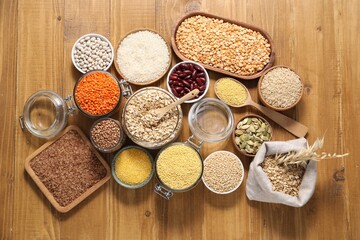 Different types of cereals, legumes and seeds on wooden table, flat lay
