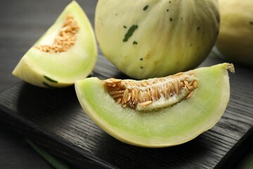 Fresh whole and cut honeydew melons on black wooden table, closeup