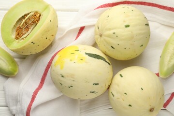 Fresh whole and cut honeydew melons on white wooden table, flat lay