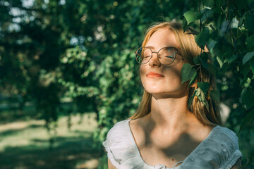 girl in glasses enjoys a quiet moment, basking in the sunlight filtering through the leaves