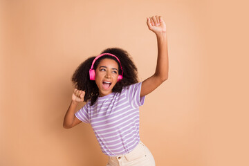 Portrait of pretty young girl dancing headphones wear striped t-shirt isolated on beige color background