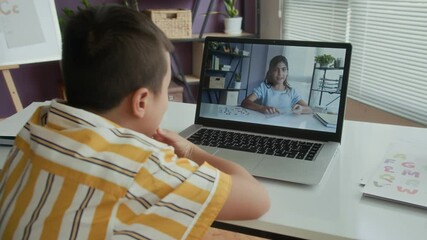 Rear view of schoolboy calling teenage girl on video during speech therapy class using wireless laptop at desk - Powered by Adobe