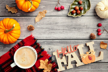 Autumn frame. Hello Fall sign, red berries, fall leaves, pumpkins, coffee cup on red plaid on wooden desk table. Flat lay, top view.