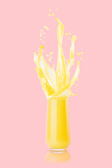 Orange juice in drinking glass with flying drops, splashes, flows of juice in motion on pink...