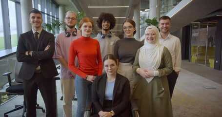 A diverse group of young business professionals stands confidently and looks into the camera in a modern business center, symbolizing ambition, diversity, and a forward-thinking corporate culture