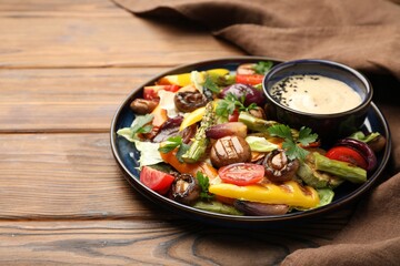 Delicious salad with grilled vegetables and sauce on wooden table, closeup