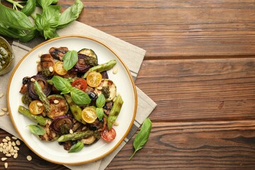 Delicious salad with grilled vegetables, basil, pesto sauce and pine nuts on wooden table, flat...