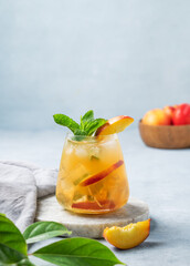 Refreshing peach cocktail, lemonade or iced tea on a marble board on a light background with leaf.