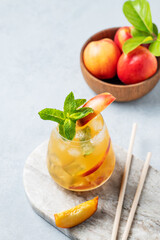 Refreshing peach cocktail, lemonade or iced tea on a marble board with tube on a light background.