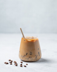 Iced coffee latte in a glass with milk on a light background with coffee beans.