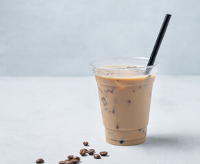 Iced coffee latte in a recyclable plastic glass with milk and ice on a light background with coffee beans.