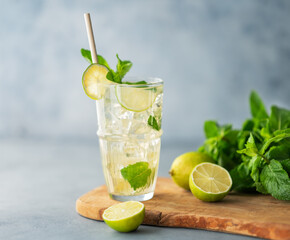 Mojito cocktail in a tall glass with lime, mint and ice on a wooden board on a blue textured...
