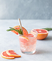 Grapefruit cocktail in a glass with rosemary and ice on a light background with fresh fruits.