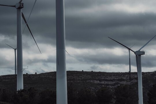 A closer perspective showcasing three large wind turbines standing tall against a dark, cloudy sky, illustrating the persistence and resilience of renewable energy sources in Tarragona Spain