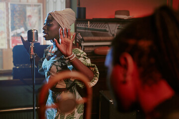 Selective focus shot of young Black woman singing jazz song in microphone during rehearsal with band