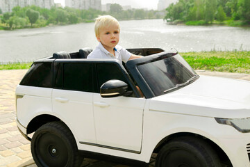 Cute funny blond little young toddler kid child boy sitting,driving,riding in electric toy car,automobile,jeep in park.Children physical,emotional development,childhood daycare,kindergarten concept.