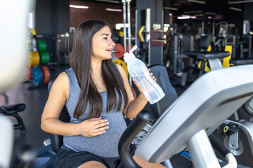 Fototapeta premium Pregnant woman in the gym with water. Sports and healthy lifestyle.