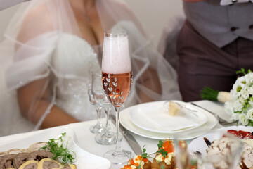 The glasses of the bride and groom are filled with sparkling wine at the festive table.