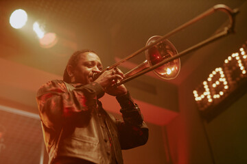 Low angle view of African American jazz musician playing trombone on stage in local bar