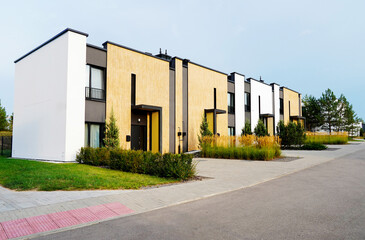 Modern townhouses in a residential area. New apartment buildings with green outdoor facilities in sustainable enviroment. Street  with Two-story townhouses. Townhouse along sidewalk with green lawn.