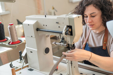 A woman tanner sews a leather belt on a sewing machine. 