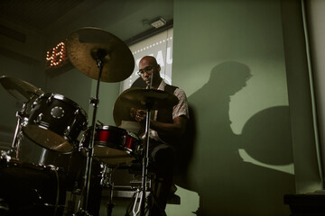 Fototapeta premium Low angle view of young Black man setting cymbal while assembling drum kit in studio, copy space