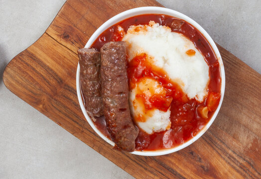 Traditional South African Pap, wors and Sheba sauce flat lay with wooden board 
on grey 
