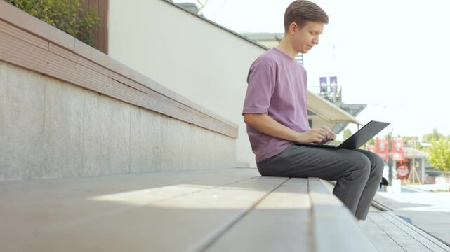 Freelancer working on laptop in the open air sitting on bench. 