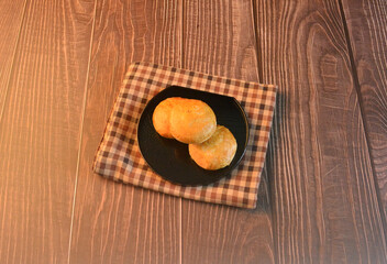 Chinese Pastry Mooncake baked round asian crispy cake with salted yellow red bean paste and eggs yolk in black plate on wood table Traditional halal menu food sweet dessert for autumn festival cafe