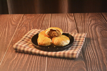 Chinese Pastry Mooncake baked round asian crispy cake with salted yellow red bean paste and eggs yolk in black plate on wood table Traditional halal menu food sweet dessert for autumn festival cafe