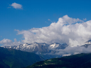 An amazing fusion of nature: green meadows at the foot of the mountains, soft clouds framing the...