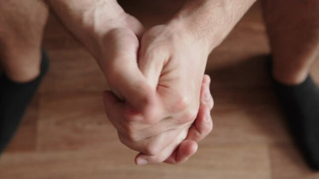Folded hands of nervous caucasian man rubbing his fingers indoors. Movements of worried, uncertain person waiting for decision. Natural motor skills of bushes, top view.