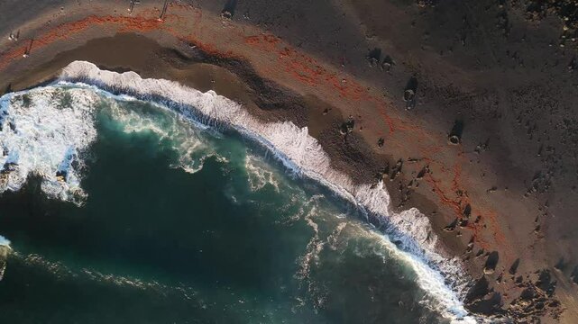 Aerial view of Volcan Bermeja and Tiny Charco Verde with a black sand beach and clear ocean waves, El Golfo, Lanzarote, Spain.