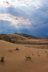 Sun rays breaking through clouds over desert dunes
