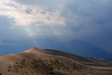 Sunlit desert dunes under dramatic clouds and sunbeams
